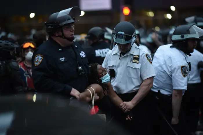 Police in riot gear twist the arms of a Black woman in custody